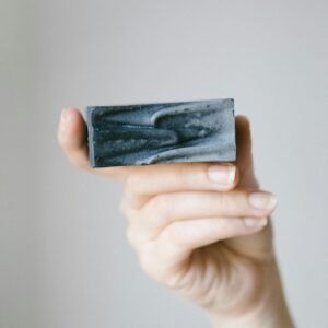 Close-up of a hand holding a black soap bar with a minimalist background.